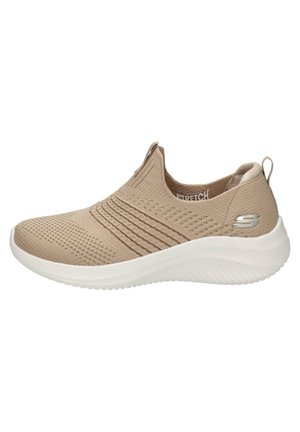 Zapato slip-on de punto beige con parte superior texturizada, collar elástico y suela de goma blanca. Presenta un pequeño logo metálico en el costado.