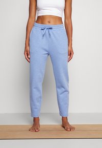 Ljust blå joggingbyxor i mjukt tyg, med resår i midjan och avsmalnande design vid anklarna. Ytan har en lätt textur.