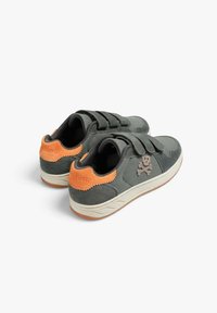 Zapatillas grises con acentos en el talón de color naranja, correas de velcro y un diseño de calavera y huesos cruzados en el lateral, expuestas sobre un fondo blanco.
