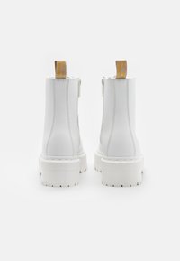 Botas de tobillo de plataforma gruesa blancas con tiradores traseros y costuras visibles, mostradas desde la parte trasera sobre un fondo blanco.
