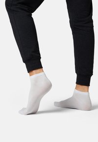 White ankle sock on a foot, shown with dark joggers. Sock has a smooth texture and a low-profile design, highlighting comfort and fit.