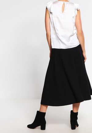 Blusa bianca con maniche a sbuffo e schiena a chiave, abbinata a una gonna midi nera fluente e stivali neri alla caviglia.