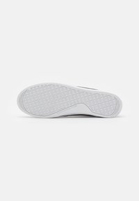 Weiße Sohle eines Sneakers mit einem rautenförmigen Profilmuster und dem eingeprägten "Tommy Hilfiger"-Logo im Bereich des Fußgewölbes auf einem schlichten Hintergrund.
