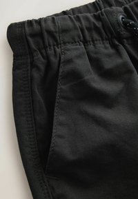 Zbliżenie czarnych spodni materiałowych z elastycznym pasem, boczną kieszenią i widocznymi detalami szwów.