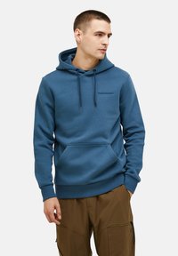 Felpa blu con cappuccio e coulisse, tasca frontale e polsini a costine. Presenta il logo "PeakPerformance" ricamato in nero sul petto.