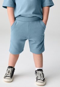 Ljusblå bomulls-t-shirt och matchande shorts med en mjuk textur, med en avslappnad passform och sidfickor, kombinerade med svarta sneakers.