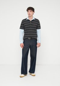 Πόλο μπλούζα με ασπρόμαυρες ρίγες πάνω από ανοιχτό μπλε μακρυμάνικη μπλούζα, συνδυασμένη με σκούρο μπλε τζιν και μπεζ αθλητικά παπούτσια· μαύρη ζώνη με στρογγυλή αγκράφα.