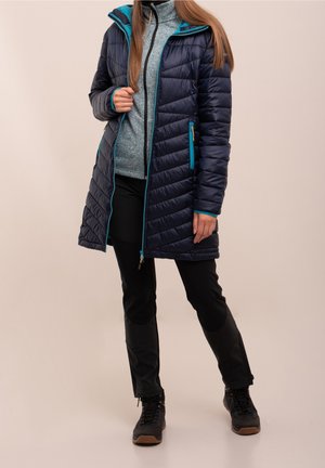 Marineblaue Pufferjacke mit türkisfarbenen Akzenten, gesteppter Verarbeitung, mit Reißverschlusstaschen und abnehmbarer Kapuze, getragen über einem grauen Fleece-Oberteil und schwarzen Hosen.