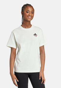 Camiseta blanca de algodón con cuello redondo y mangas cortas. Pequeño logo negro y rojo en el lado izquierdo del pecho. Textura suave y lisa.
