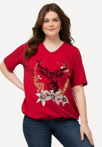 Camiseta corta roja con mangas cortas que presenta un gráfico de ciervo en negro y dorado rodeado de acentos florales. Diseño de cuello en V, tejido suave y corte relajado.