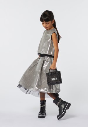 Zilver metallic cropped top en rok, met een zwarte tule onderlaag, gecombineerd met zwarte enkelboots en een kleine zwarte handtas.