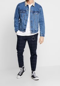 Džínová bunda s manšestrovým límcem, doplněná o námořnicky modré kostkované kalhoty a černé vysoké tenisky s bílými detaily.