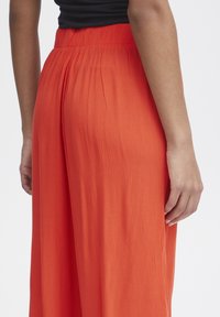 Lösa oranga byxor i texturerad tyg med en rynkad midja och ett flödande silhuett, fångade från sidan.