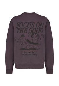 Lila Sweatshirt mit rundem Halsausschnitt, verziert mit schwarzen Grafiken, die sagen: "KONZENTRIERE DICH AUF DAS GUTE" und "Das Leben ist zu kurz, um es ernst zu nehmen."