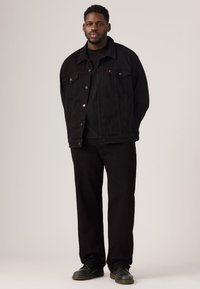 Black denim jacket with chest pockets, paired with a black t-shirt and loose-fit black pants. Black shoes complete the outfit.