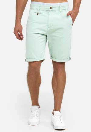 Pantalones cortos de algodón verde menta con puños doblados, bolsillos frontales y cierre de botón. Combinados con zapatillas blancas.