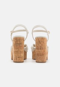 Sandales blanches à plateforme avec des talons en liège et des brides de cheville. Le talon présente un motif en liège texturé avec une finition brillante.