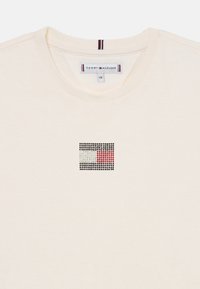 Kremfarget bomulls-t-skjorte med et rektangulært logo dekorert med rhinestones i rødt, hvitt og svart, og med ribbestrikket hals.