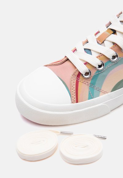 Κοντινό πλάνο ενός παπουτσιού αθλητικού με ρίγες σε παστέλ χρώματα του ουράνιου τόξου, λευκό κάλυμμα στα δάχτυλα, λευκά κορδόνια περασμένα και ένα επιπλέον ζευγάρι λευκών κορδονιών δίπλα του.