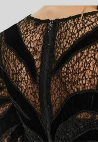 Abito in pizzo nero con motivo floreale, dettagli in velluto e chiusura con cerniera sul retro. Tessuto testurizzato con dettagli intricati.