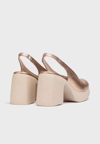 Zapatos de plataforma tipo slingback con parte superior texturizada en oro rosa metálico y un tacón grueso en color beige. Forro interior suave y correa ajustable.