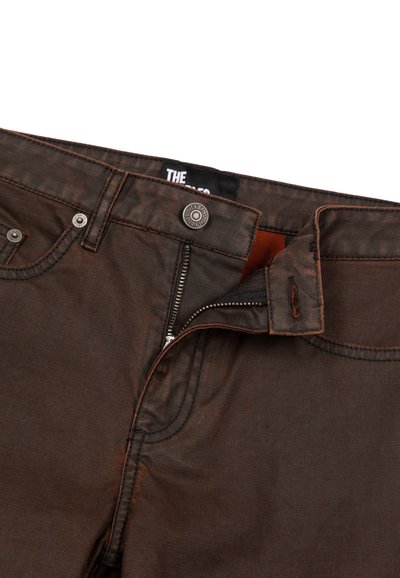 Jean en denim marron avec une fermeture éclair, un bouton et une doublure intérieure orange. Présente une couture contrastante et un design classique à cinq poches.