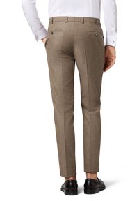 Braune maßgeschneiderte Hose mit strukturiertem Finish, schlanker Schnitt und zwei Gesäßtaschen mit Knopfverschluss. Getragen mit schwarzen Schuhen und einem weißen Hemd.