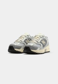 Een paar grijze en witte New Balance hardloopschoenen met details van mesh en suede, lichte beige tussenzolen en zwarte rubberen buitenzolen, in een schuine voorkantweergave.