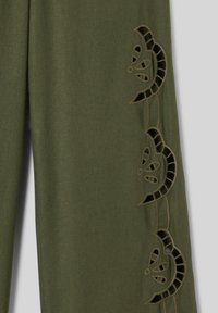 Tissu vert olive avec des motifs floraux découpés verticalement le long d’un bord, montrant des formes complexes de pétales et de courbes.