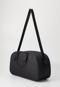 Borsa a duffle nera con forma arrotondata, materiale in tessuto, doppie maniglie e una tracolla regolabile. Presenta una chiusura con zip e nessun motivo visibile.