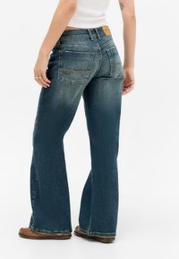 Wijd uitlopende denim jeans in donkerblauw met een vervaagde textuur. Bevat achterzakken en een tan leren label bij de tailleband.