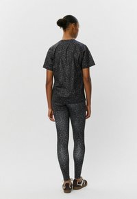 Súprava čierneho trička s leopardím vzorom a legín, ktorá má priliehavý strih a hladkú textúru. Hnedé šnurovacie topánky dotvárajú celkový vzhľad.