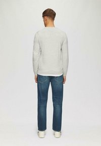 Grauer Sweatshirt mit Rundhalsausschnitt, kombiniert mit blauen Jeans. Die Jeans haben einen klassischen Schnitt und sind an den Knöcheln leicht tailliert.