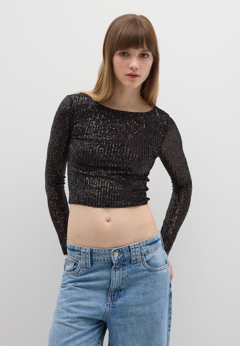 Schwarzes, langärmeliges, bauchfreies Oberteil mit Pailletten und rundem Ausschnitt, kombiniert mit hellblauen, hoch taillierten Jeans mit Fronttaschen.