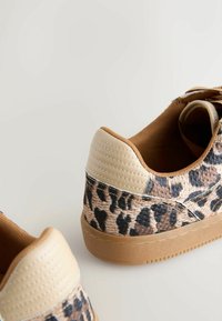 Paire de baskets basses à imprimé léopard marron et beige, talon rembourré beige et semelle en caoutchouc marron clair sur une surface blanche.