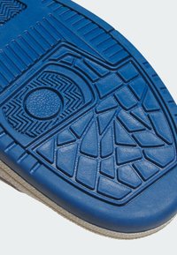 Plavi gumeni potplat cipele s geometrijskim uzorcima opipa, uključujući krugove, linije i trokutaste oblike na bijeloj pozadini.