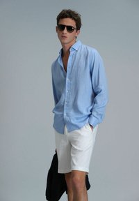 Himmelblaues Leinen-Hemd mit Knöpfen, weiße Shorts und schwarze Sonnenbrille, die ein lässiges Outfit mit lockerer Passform und weicher Textur zeigt.