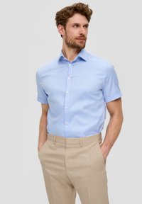Jasnoniebieska koszula z krótkim rękawem z kołnierzykiem button-down i delikatnym wzorem w paski, połączona z beżowymi spodniami fasonu tailor. Gładka tekstura materiału.