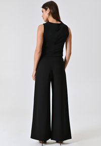 Zwarte mouwloze jumpsuit met een aansluitend lijfje en brede broekspijpen. Gladde stof, minimalistisch ontwerp en zichtbare naaddetails aan de achterkant.