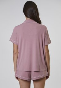 Kort rosa pyjamas-set i mjukt tyg. Toppen har en krage och korta ärmar, och shortsen har vit kant och en avslappnad passform.