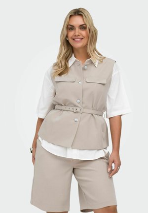 Frau trägt eine beige ärmellose, taillierte Weste über einem weißen Kurzarmhemd und passende beige Shorts bis zum Knie, lächelt mit offenem blondem Haar.