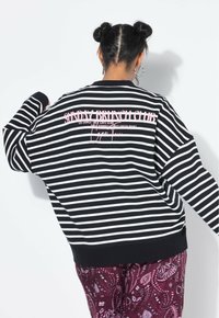 Sweatshirt rayé noir et blanc à manches longues, avec le texte rose "SUNDAY BRUNCH CLUB" au dos, associé à un pantalon bordeaux à motifs.