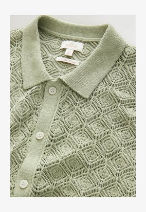 Polo shirt tricoté vert clair avec un motif géométrique texturé, doté d'un col, de cinq boutons et d'une étiquette indiquant la taille M.