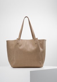 Beige nahkakassi, jossa on kaksi tukevaa kahvaa, pehmeä tekstuuri ja yksinkertainen, tilava muotoilu, ihanteellinen päivittäiseen käyttöön.