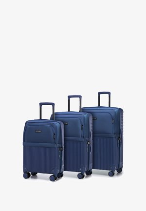 Three navy blue suitcases in graduated sizes, featuring a smooth top section and textured ribbed bottom, all with retractable handles and spinner wheels.