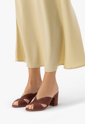 Stopy w brązowych zamszowych sandałach na słupku, z odkrytymi palcami, zestawione z kremową, zwiewną spódnicą midi.