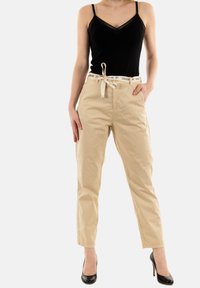 Zwarte tanktop met kantdetails, gecombineerd met beige, hoge taille broeken met een trekkoord en zwarte tekst op de tailleband.