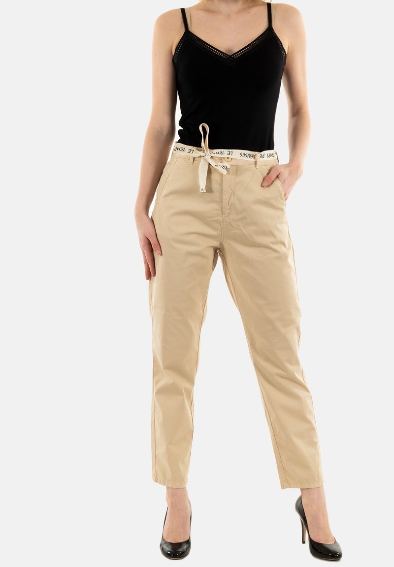 Zwarte tanktop met kantdetails, gecombineerd met beige, hoge taille broeken met een trekkoord en zwarte tekst op de tailleband.