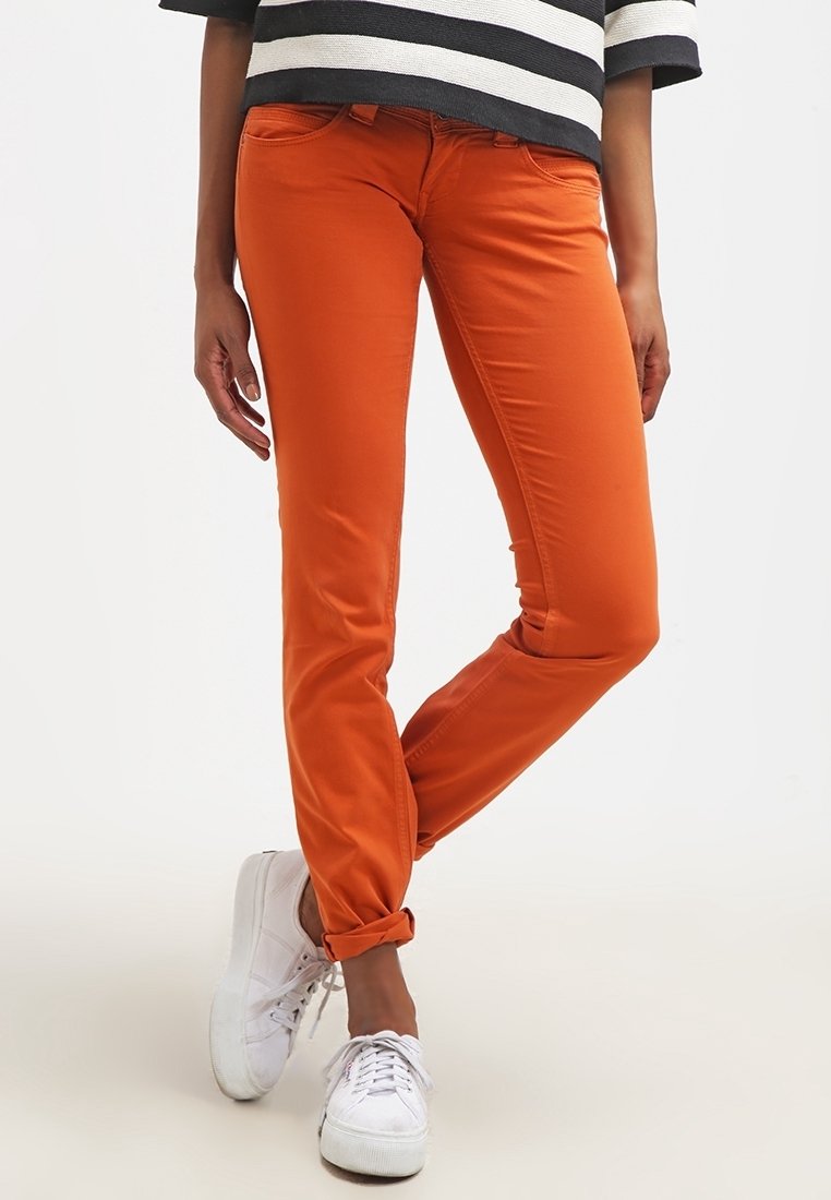 Personne portant un pantalon slim orange vif roulé aux chevilles avec des baskets blanches et un haut rayé noir et blanc.