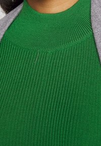 Haut vert en maille côtelée avec un col montant et une finition texturée ; présente une coupe ajustée et une légère variation dans le motif de la maille.